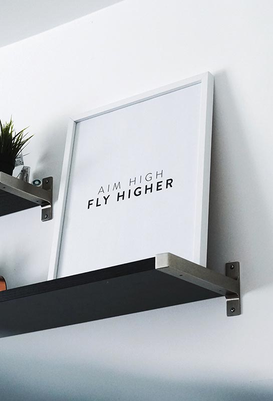 Affiche posée sur une étagère et sur laquelle il est écrit Aim high fly higher